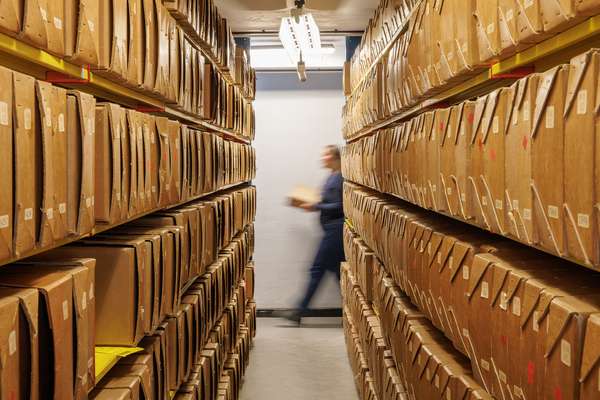 An archivist walks past shelves full of archival boxes.