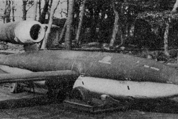 Photograph of a V1 bomb, the size and shape of a small jet aircraft, on a wheeled base on the ground.