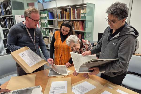 Four people of different ages are engrossed reading copies of historical documents around a table.