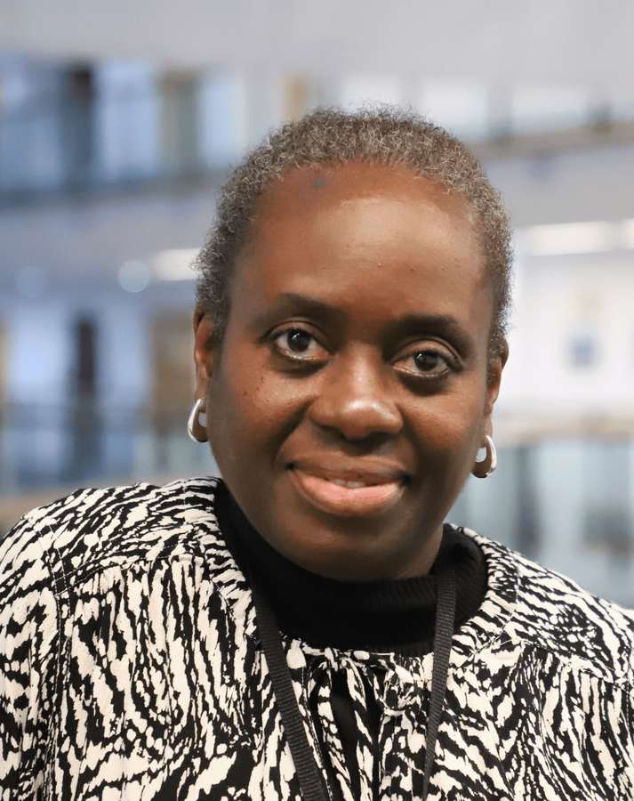 Tobi is smiling and looking directly into the camera. She is wearing a black and white patterned blouse.