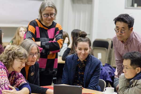 A group of people at a workshop gather round a table looking at a tablet.