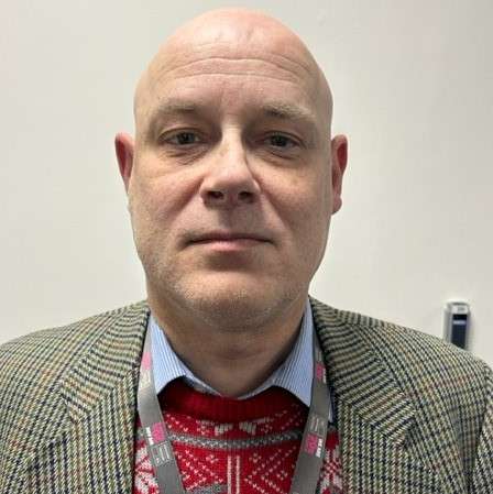 James is wearing a Christmas jumper under a beige checked blazer