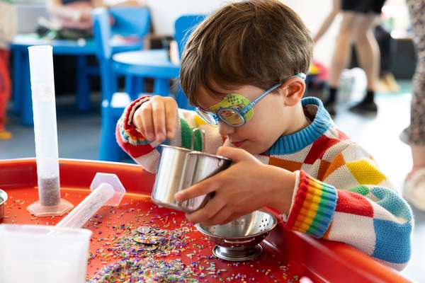 A child plays with piles of colourful rice using pots, pans and test tubes.