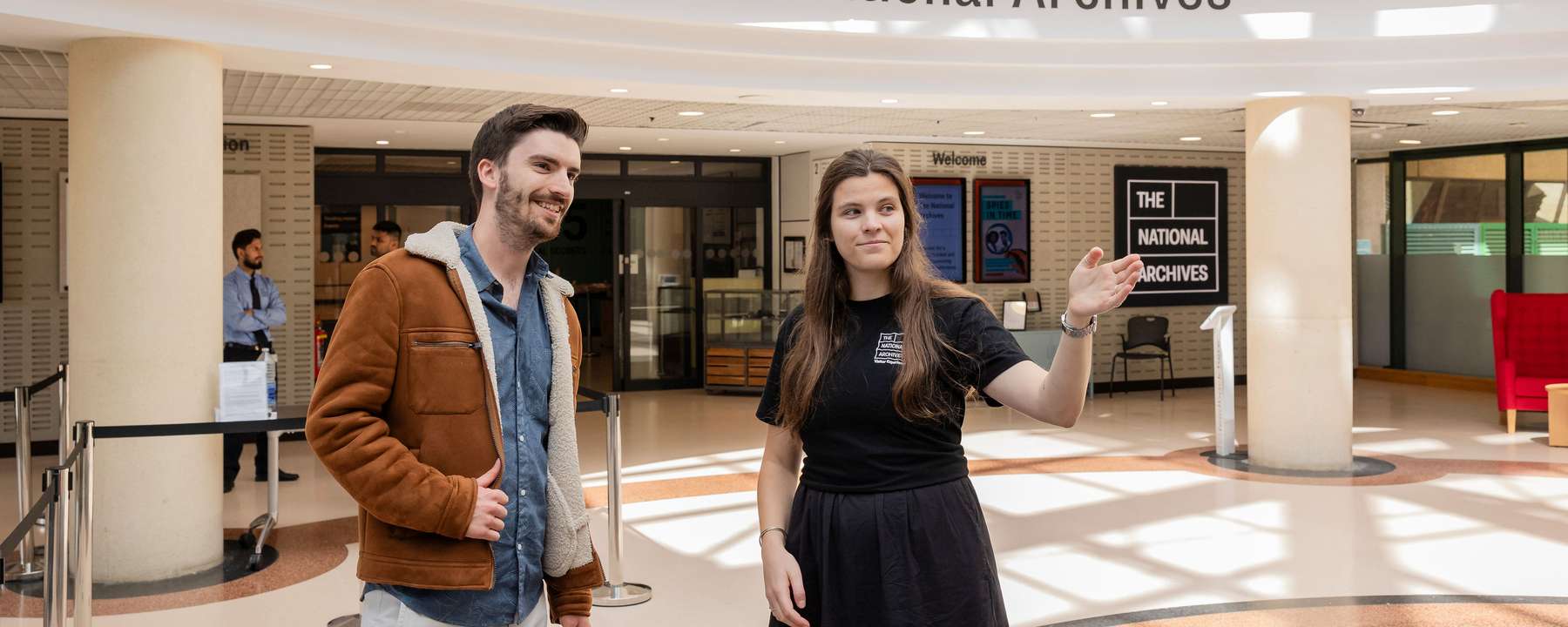 A member of National Archives staff greets a visitor in the welcome hall, a large airy space.