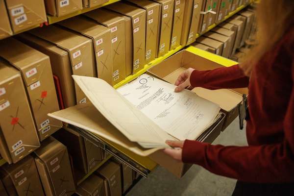 person looking at white documents in a brown box file in our Repositories