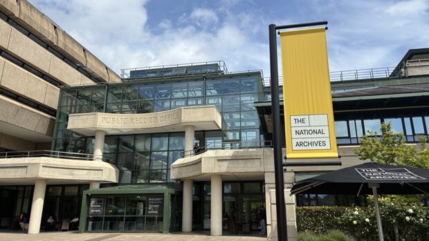 Exterior of The National Archives building in Kew, showing the entrance with “Public Record Office” signage and a yellow National Archives sign