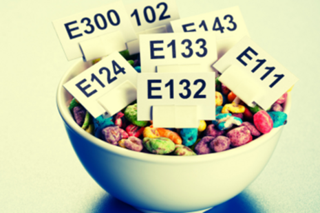 A bowl of colourful cereal, with small signs on top naming different e numbers.