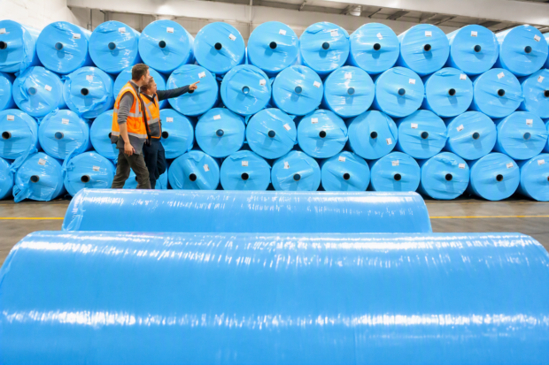 2 workers at Welsh business Concrete Canvas with large wrapped blue plastic rolls of product wrapped in their warehouse