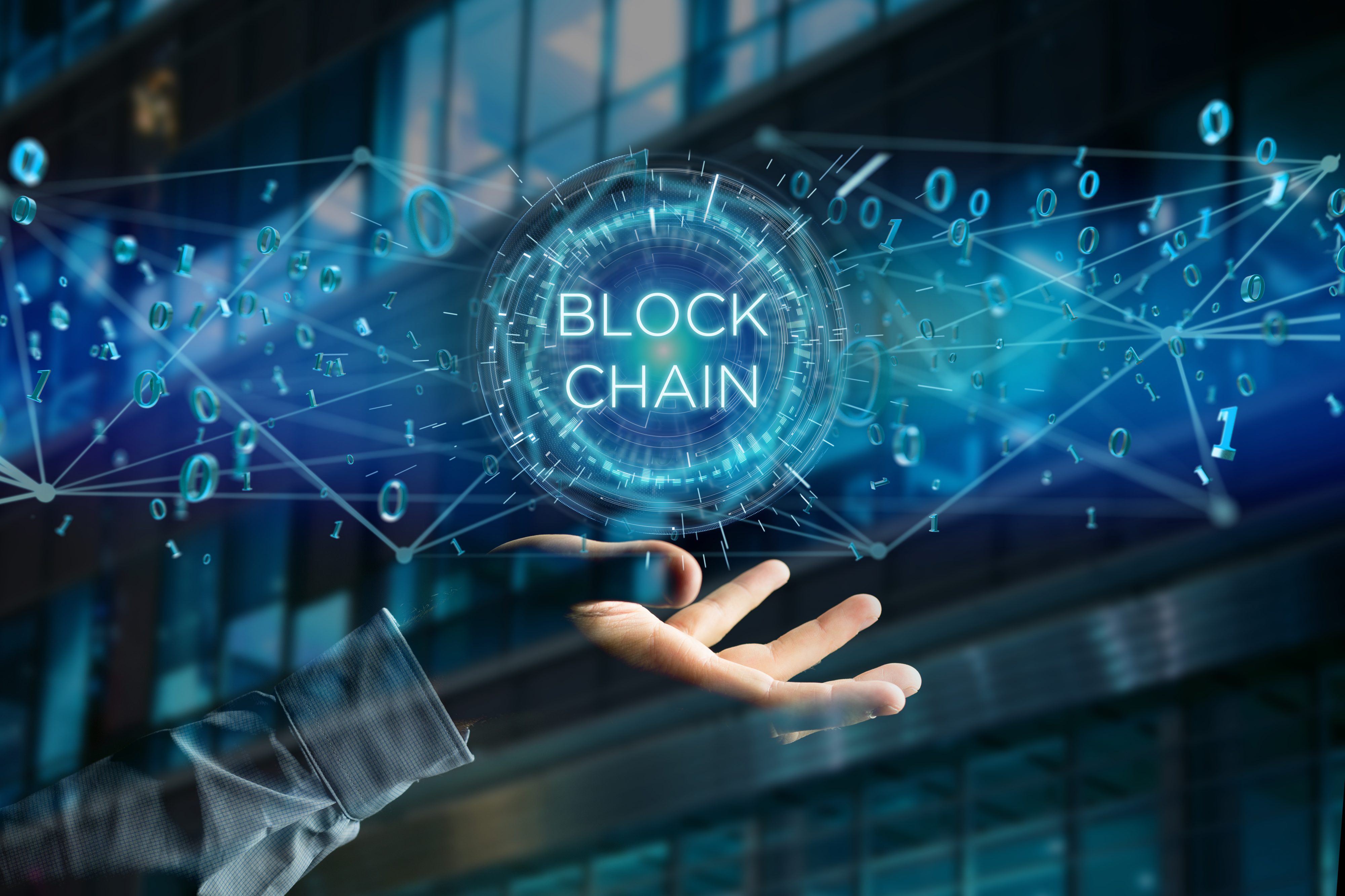 Image of man's hand balancing the word blockchain in a graphic display of 1s and 0s.