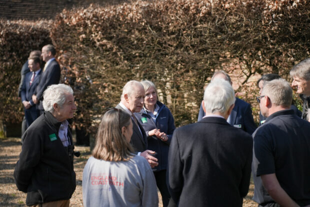 A group of people in Natural England and England Coast Path uniform in conversation with King Charles III in a walled garden.