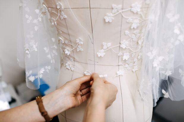 Work process of a tailor in her studio, hands sewing a wedding dress.
