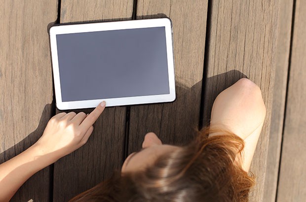 Image of a blank tablet on wood decking being read by a female.