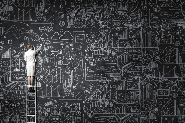 Rear view of woman standing on ladder and drawing science sketch on wall