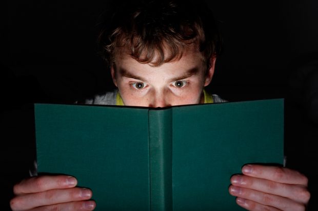 Young man reading a book at night looking intrigued