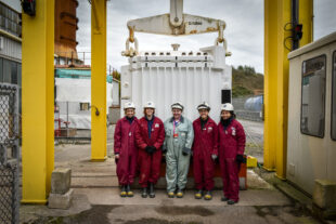 Employees standing in front of a flask leaving Calder Hall