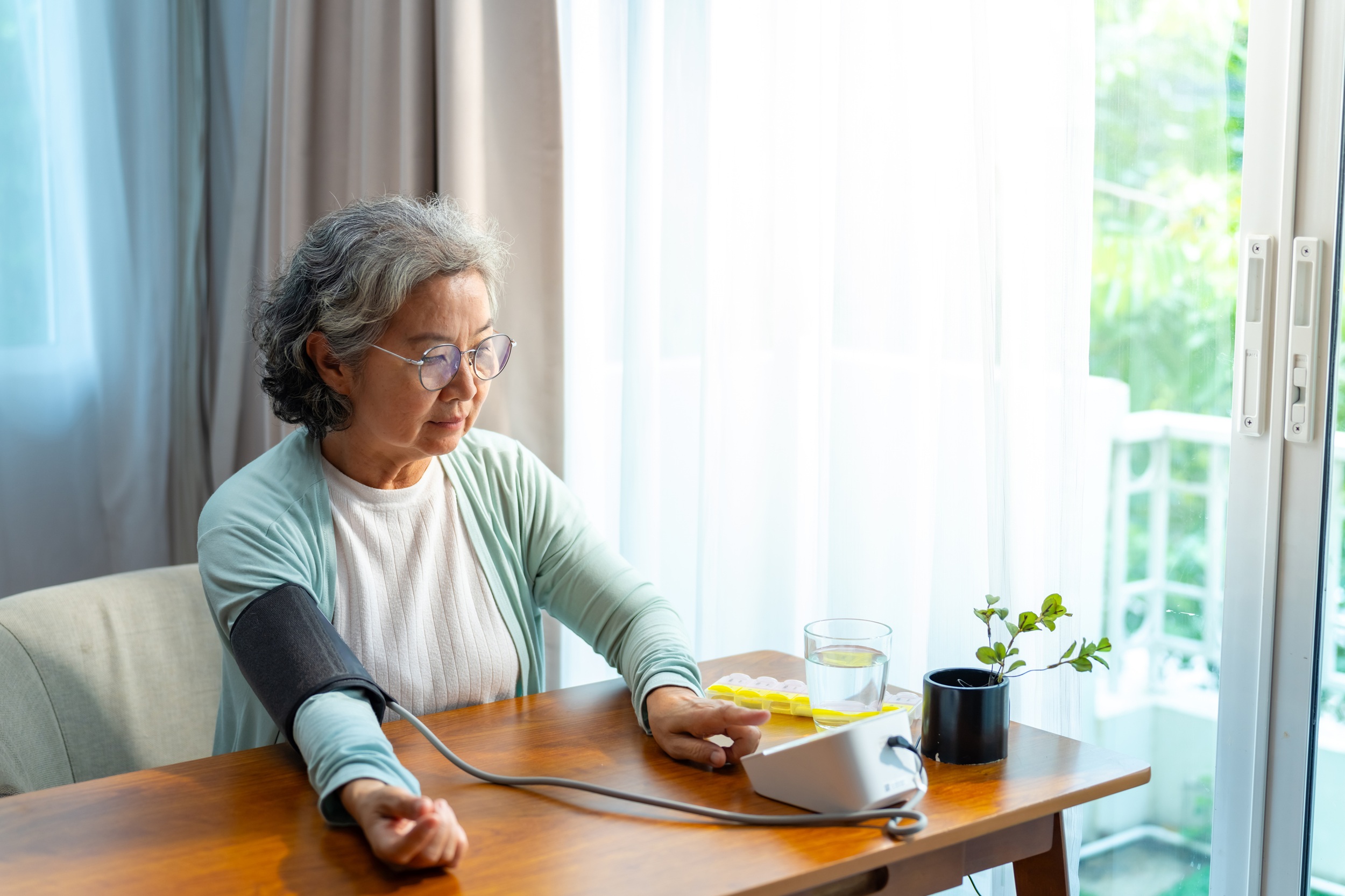 Older woman checks her own blood pressure at home using a machine. Credit: iStock Photo