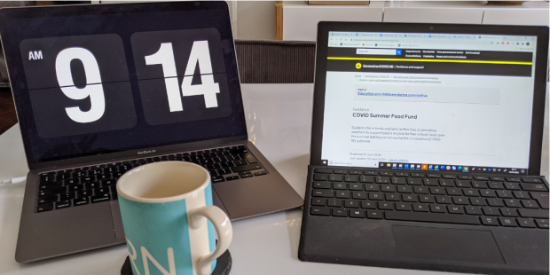 A desk with two monitors. One with GOV.Uk page featuring content about Covid summer school fund and the other with a timer screen saver on.