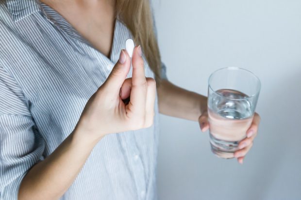 girl holding a pill and a glass of water