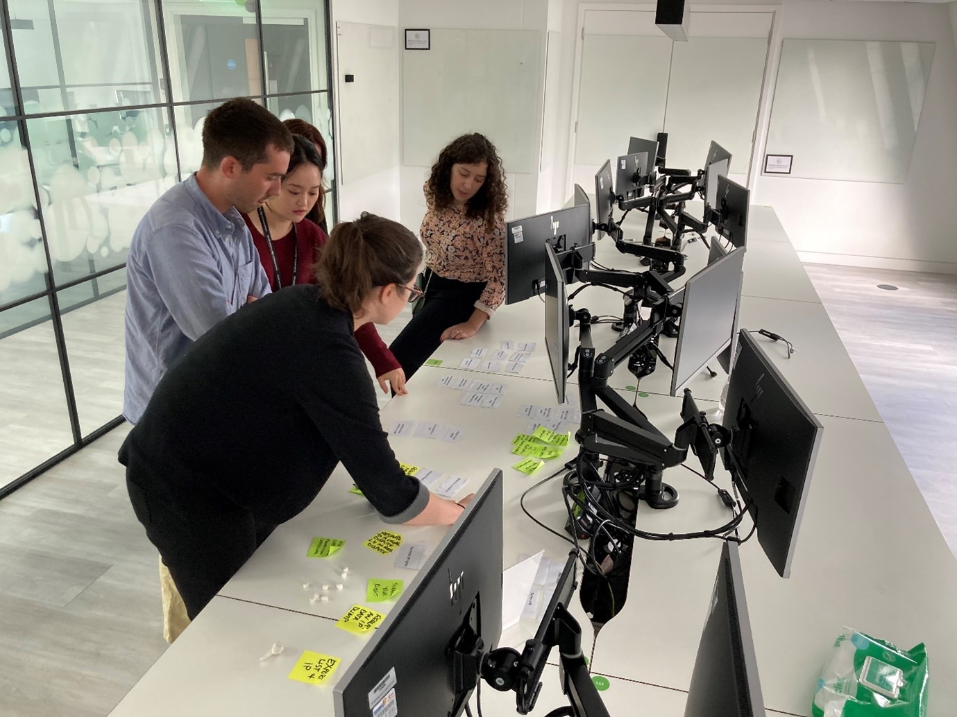 People standing at desk with computer monitors looking at paper