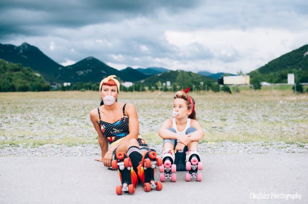 Woman and young girl sat on side of road wearing roller skates, blowing bubbles.