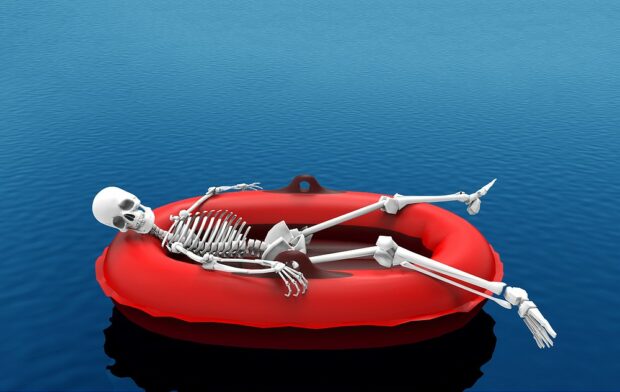A human skeleton bone lying on red life rescue boat floating on blue water.