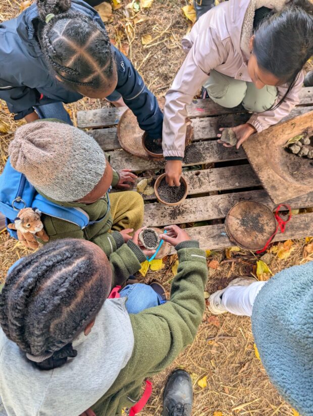 Photo taken from above of children in hats and coats at a wooden table outside, making seed bombs for swifts.