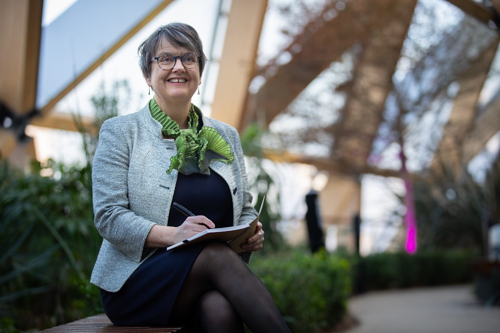 Fiona Dunsire - Go vernment Actuary sits on bench near plants with a pen and notebook.