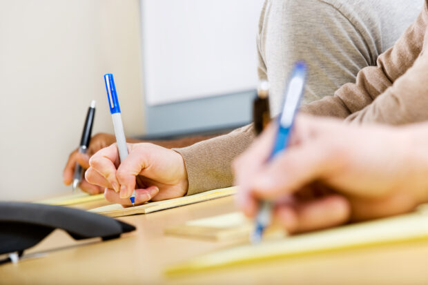 Students take notes on paper.