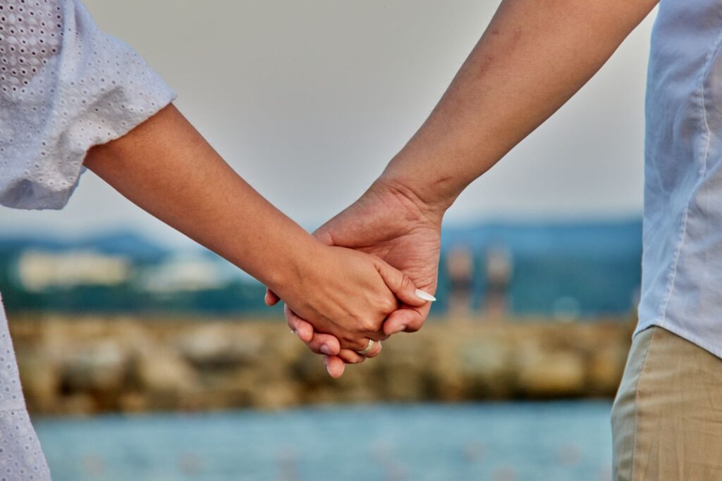A couple holding hands against a blurred background showing water and rocks