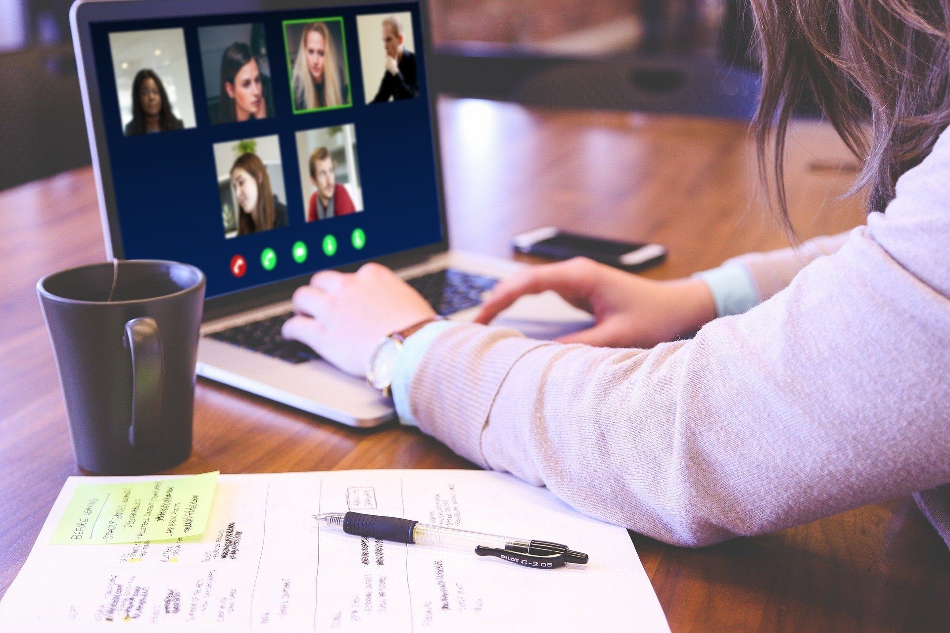 Woman typing on a laptop on which there are images of several people taking part in a webinar.