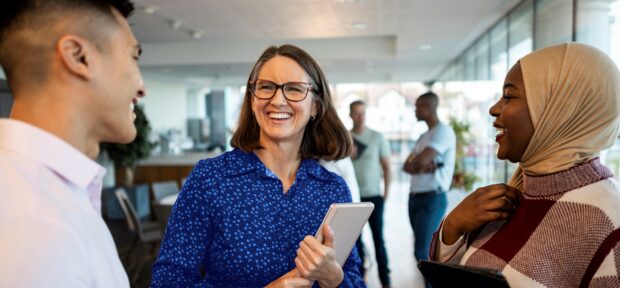 Colleagues standing in an office, smiling and speaking to each other