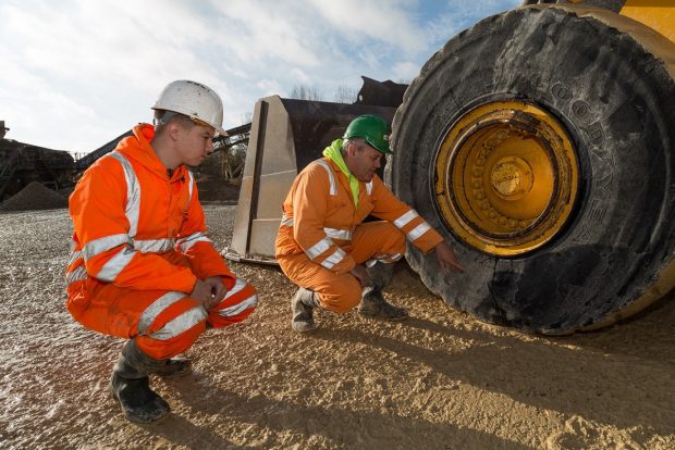An apprentice Mineral Processing Mobile and Static Plant Operator crouching down with colleague next to mobile heavy plant vehicle
