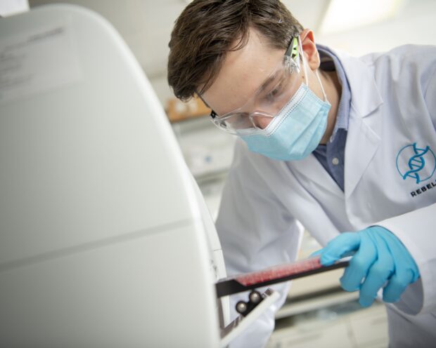 person with brown hair with mask and clear glasses white coat