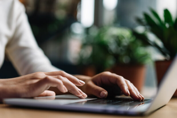 A side view of a persons hands typing on a laptop