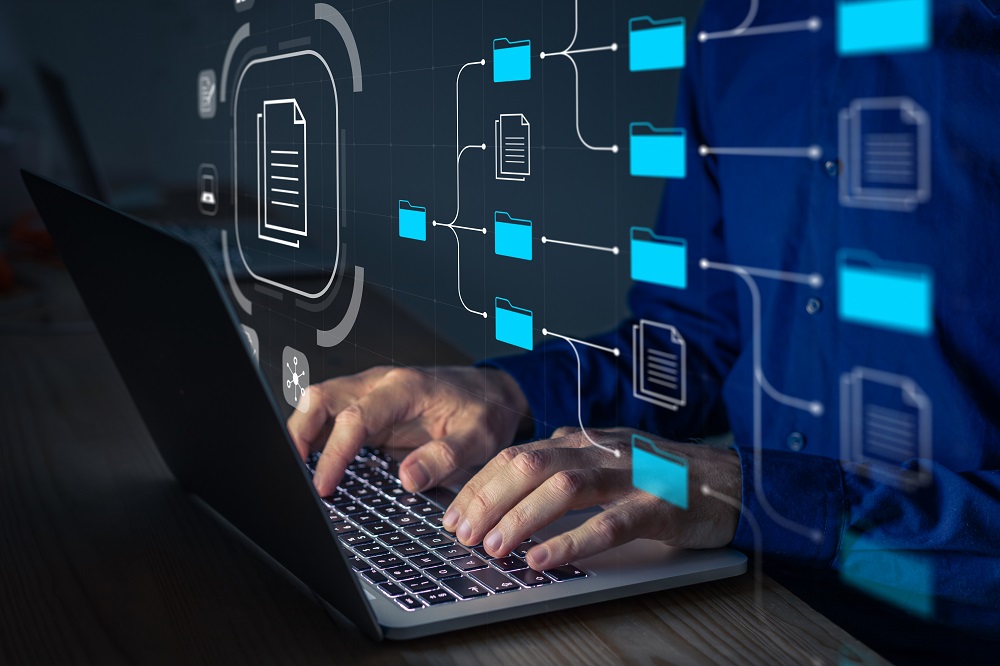Hands type on the keyboard of a laptop. Superimposed above those are images of a file management system. Credit: Shutterstock