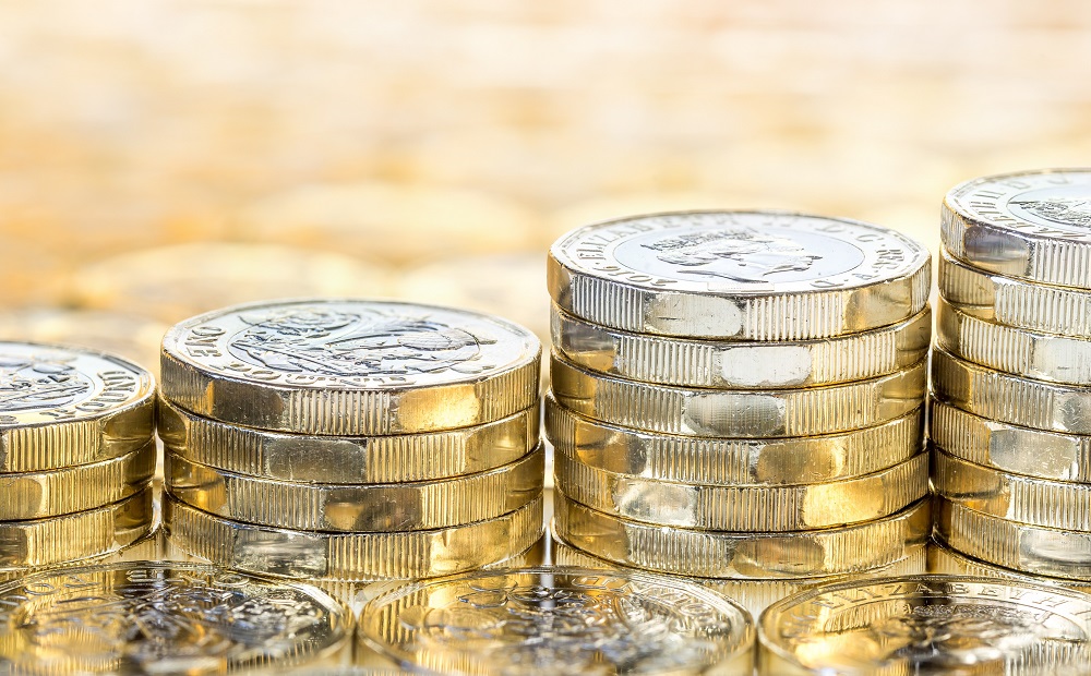 Ascending stacks of shiny pound coins on a light orange background.