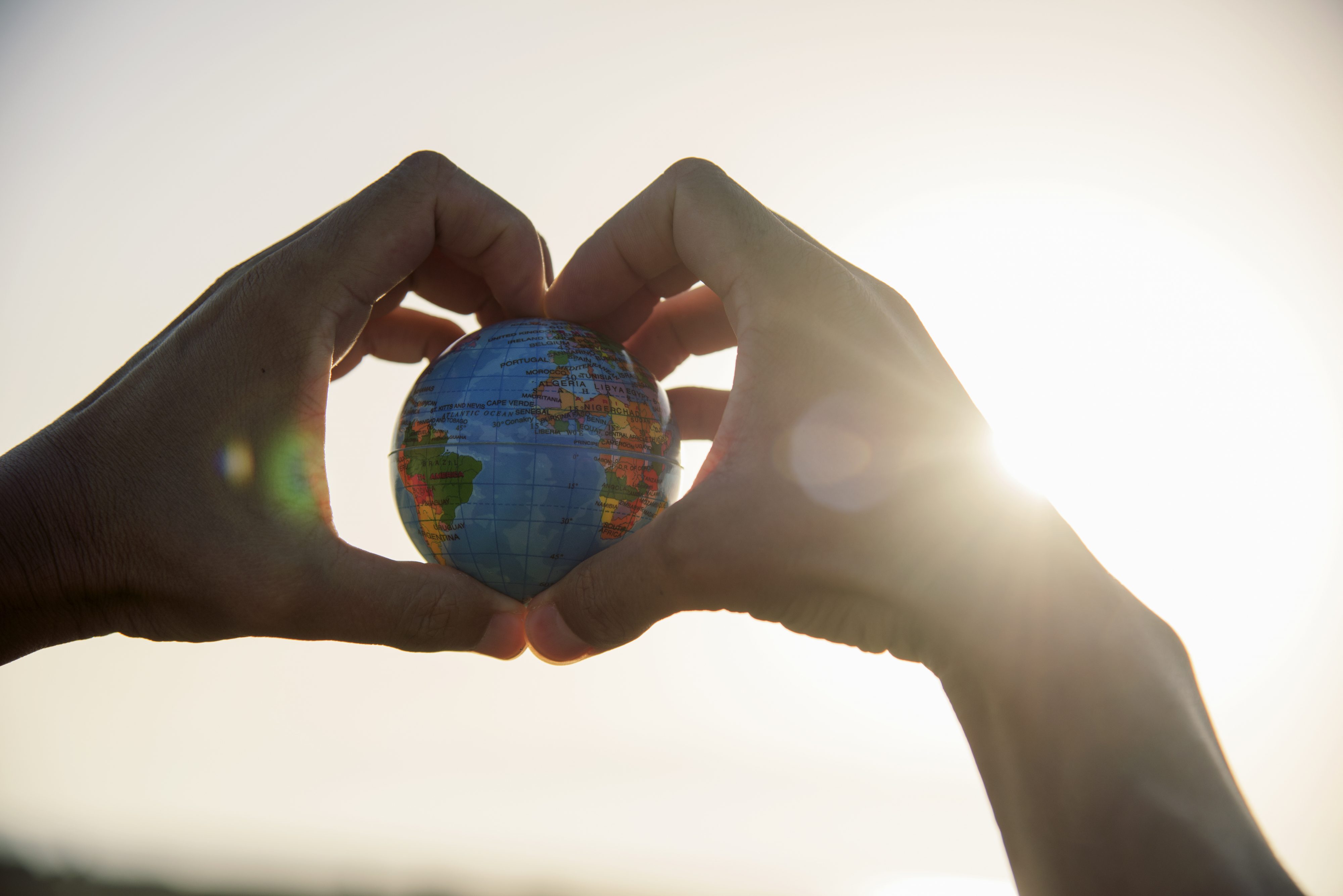 Two hands holding a small Earth globe with sun in the background