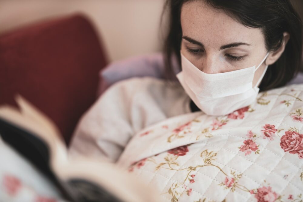 Woman wearing face mask sits on sofa and reads a book. Credit: Engin Akyurt, Unsplash.