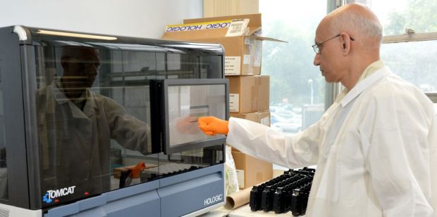 A man with a white coat works busily in a lab.