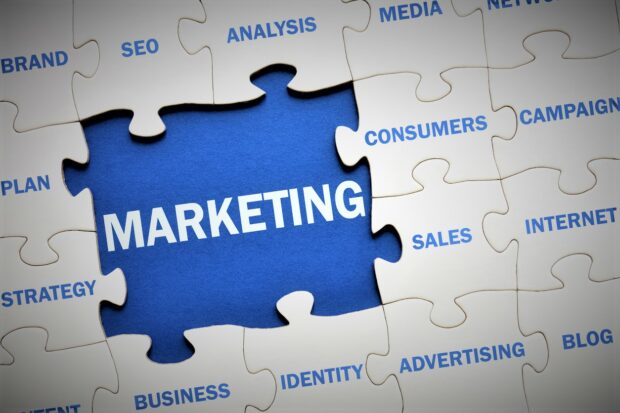 Jigsaw image with words commonly associated with sales and marketing on the pieces. There is a missing piece that shows a blue background and the word marketing.
