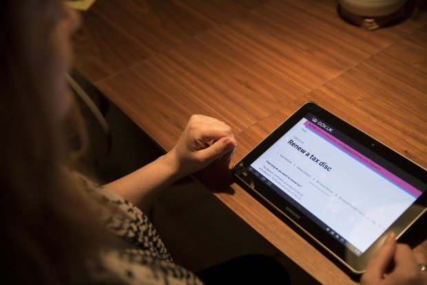 A woman sitting at a table using a tablet device. The page is loaded to the "renew a tax disc'" service