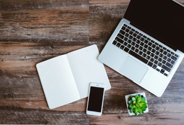 Flat lay photo of workspace desk with laptop, smartphone, blank notebook and green plant