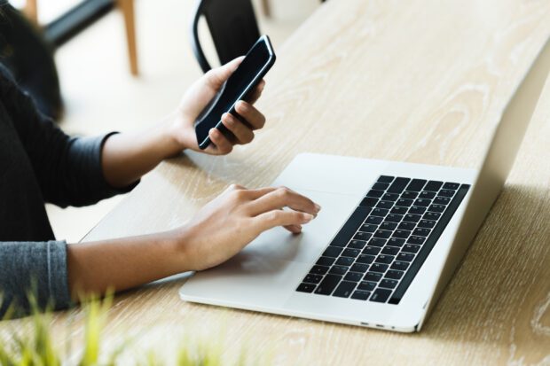 Person using laptop and phone in other hand on a desk