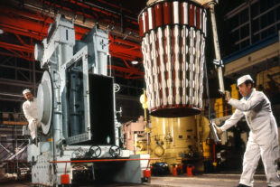 Fuel rods being lowered into the reactor at Calder Hall by 2 men dressed in white coveralls