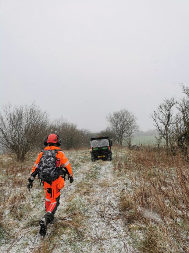 One of the team walking back towards the van. They are wearing high visibility safety gear. There is a light snow on the ground.
