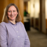 An image of Sue Bateman smiling at the camera with a blurred office corridor in the background.
