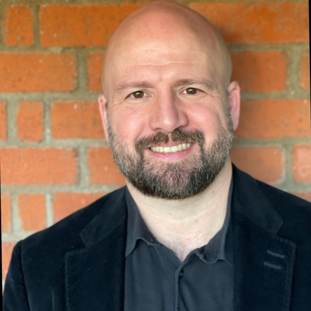 A photo of Charles Baird smiling at the camera with a brick wall behind him