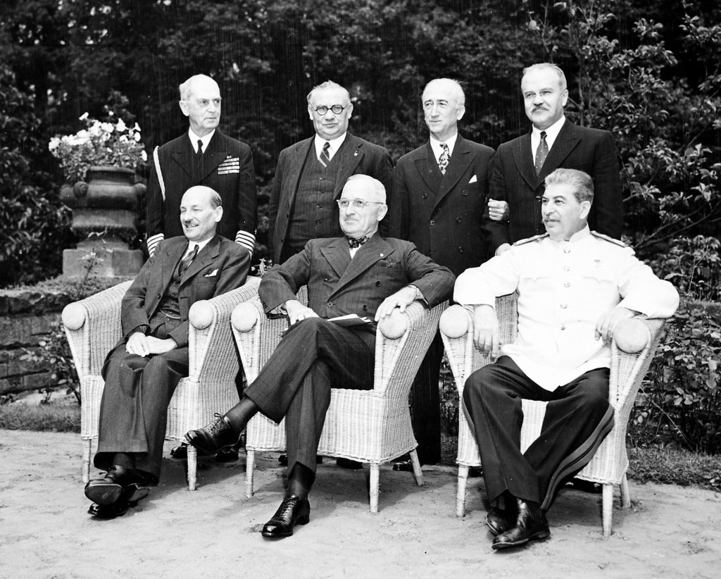 Seated in the garden of Cecilienhof Palace in Potsdam, Germany, L to R: British Prime Minister Clement Attlee, President Harry S. Truman, and Soviet Prime Minister Josef Stalin. L to R, behind them: Adm. William Leahy, British foreign minister Ernest Bevin, Secretary of State James Byrnes, and Soviet foreign minister Vyacheslav Molotov. They are all attending the Potsdam Conference.