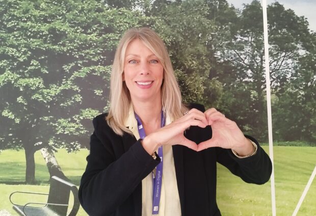 Image of a blonde female striking a heart pose for International Women's Day.