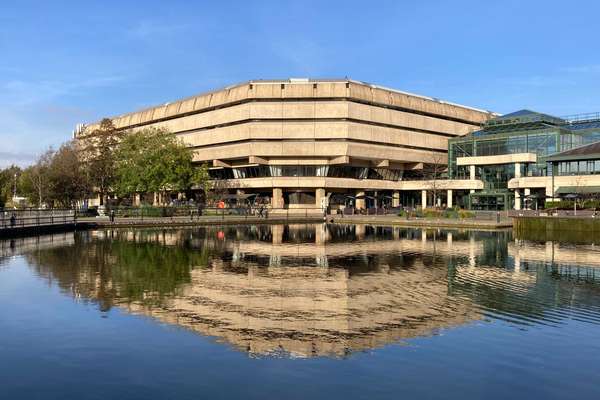 The brutalist main building at The National Archives, Kew, reflected on the water of the lake beside it.